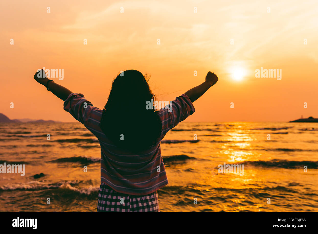Il successo o il concetto di libertà. ragazza si elevano due mano guardando il tramonto sul mare. Foto Stock