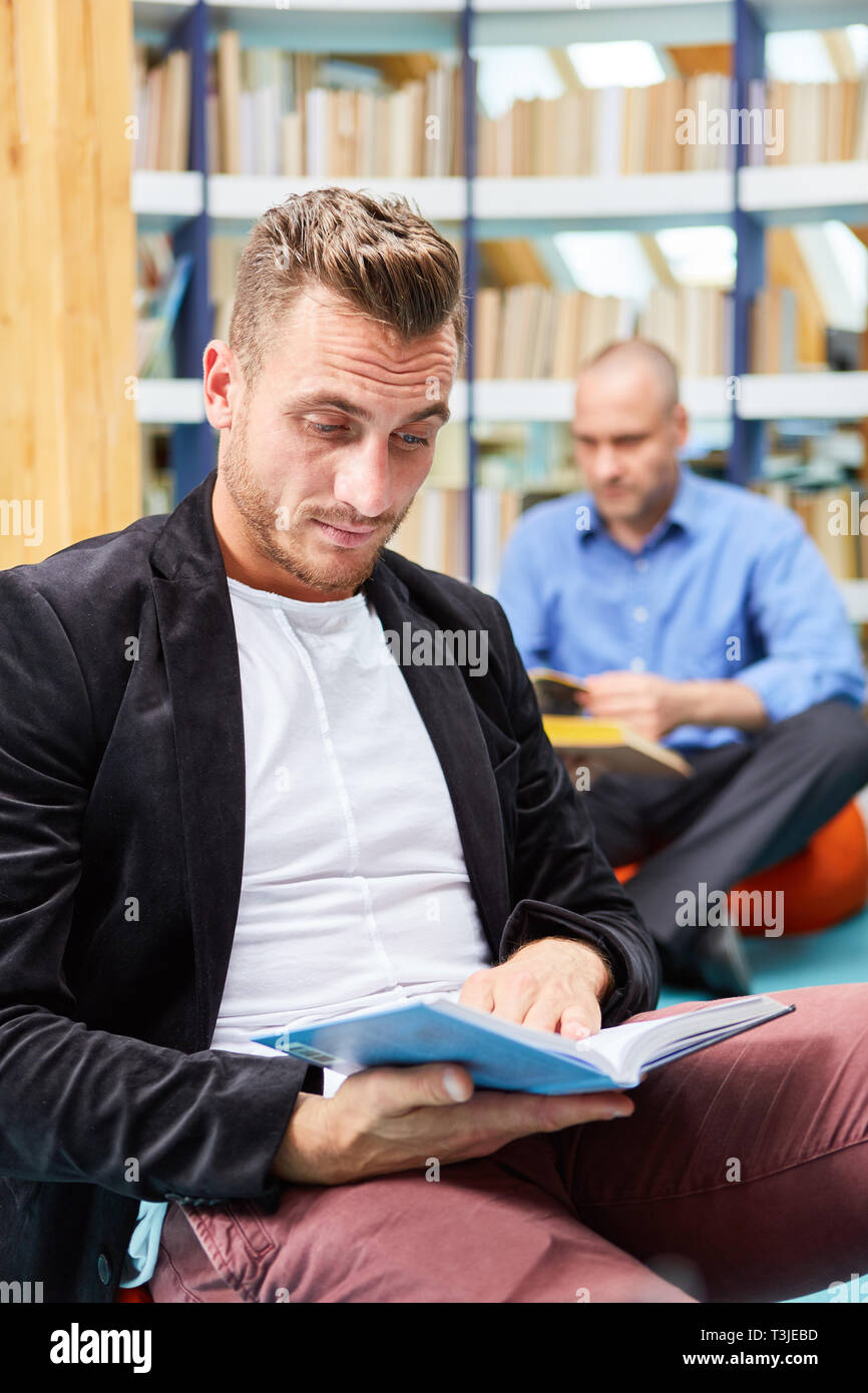 Giovane uomo legge concentrati in un libro nella biblioteca della community college Foto Stock