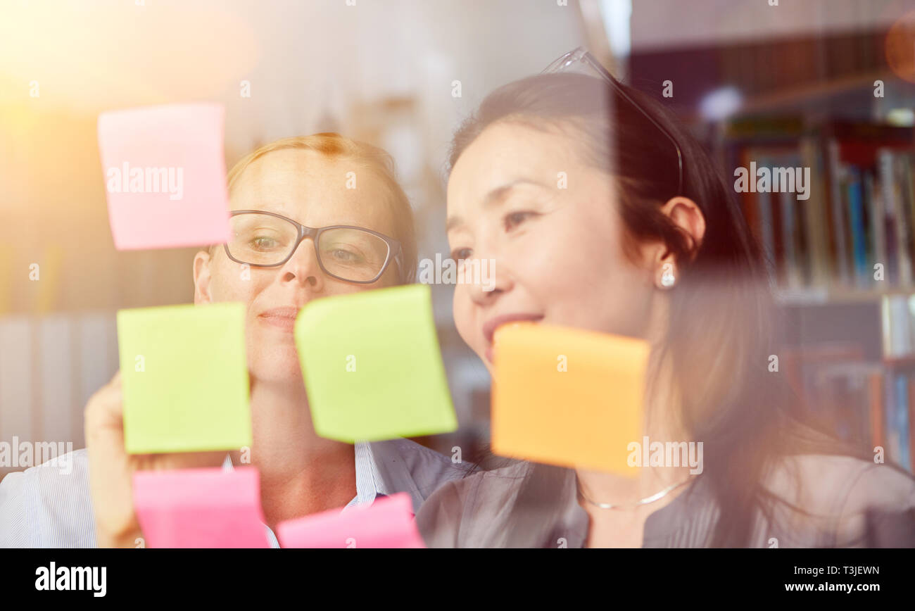 Le donne d'affari di fronte sticky notes durante il brainstorming creativo in officina Foto Stock