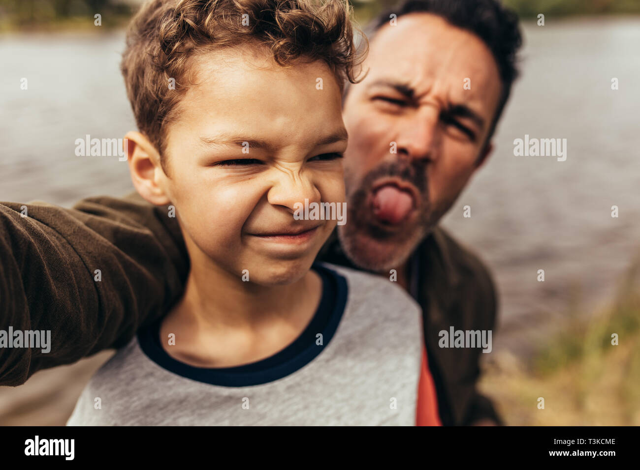 Close up di un bambino in piedi vicino a un lago con suo padre a fare ritratti in piedi dietro di lui. Padre e figlio di trascorrere del tempo insieme divertimento all'aperto. Foto Stock