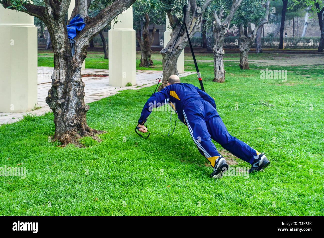 L'uomo allena il suo corpo sotto gli ulivi, Turia Gardens Valencia Spagna che si esercita nel parco europeo stile di vita fitness Foto Stock