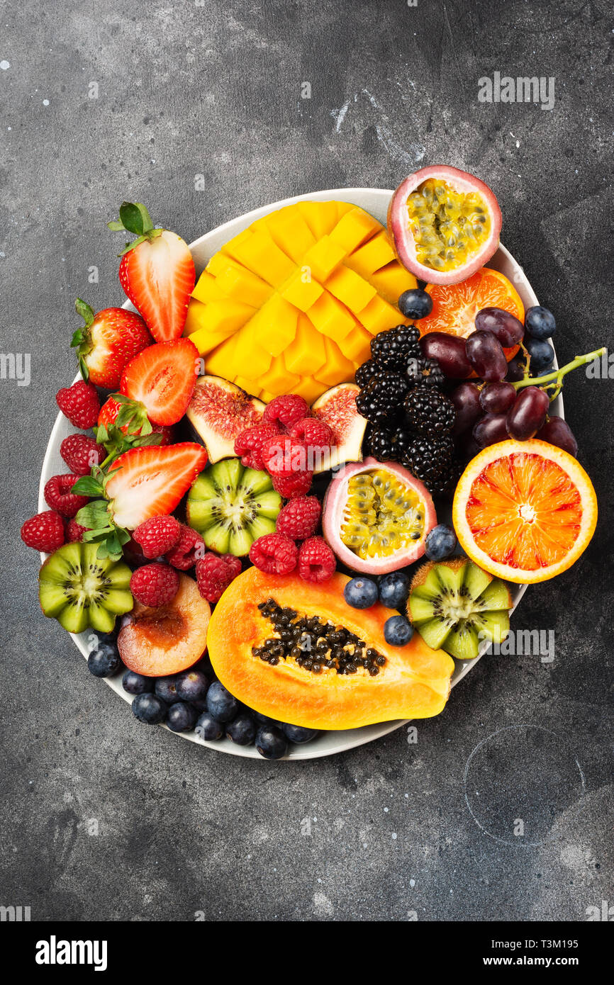 Deliziosa frutta mango papaia arance passione frutti in bacche di forma ovale piatto sul calcestruzzo scuro sfondo, vista aerea, il fuoco selettivo Foto Stock