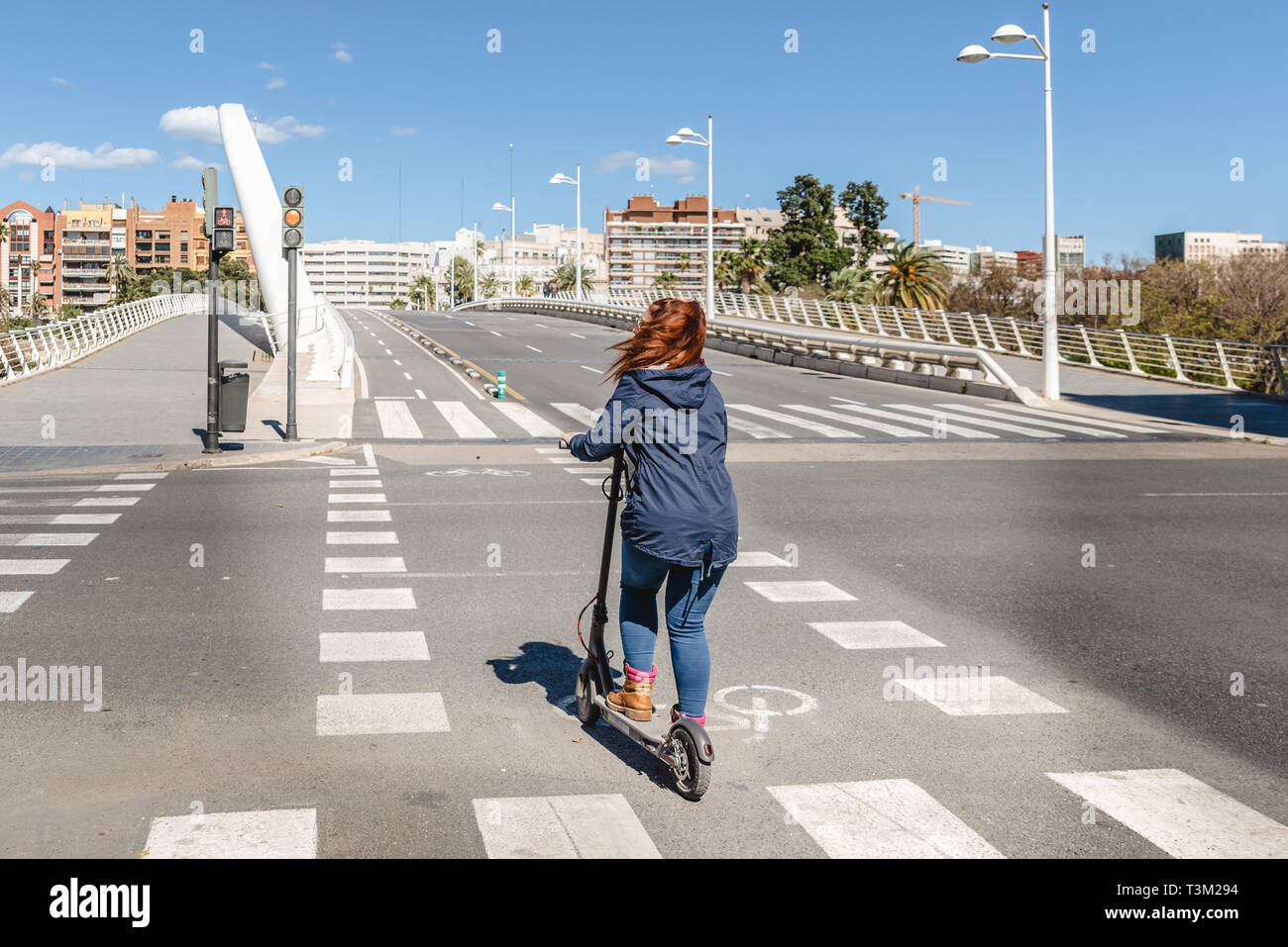 Donna su scooter elettrico attraversare una strada senza automobili su di una pista ciclabile nella città di Valencia. Foto Stock