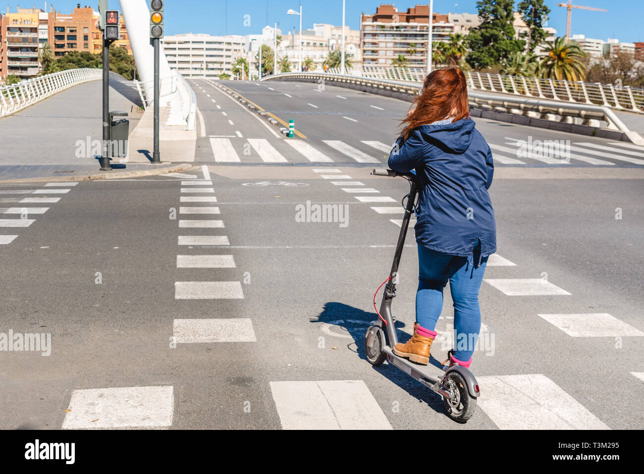 Donna su scooter elettrico attraversare una strada senza automobili su di una pista ciclabile nella città di Valencia. Foto Stock