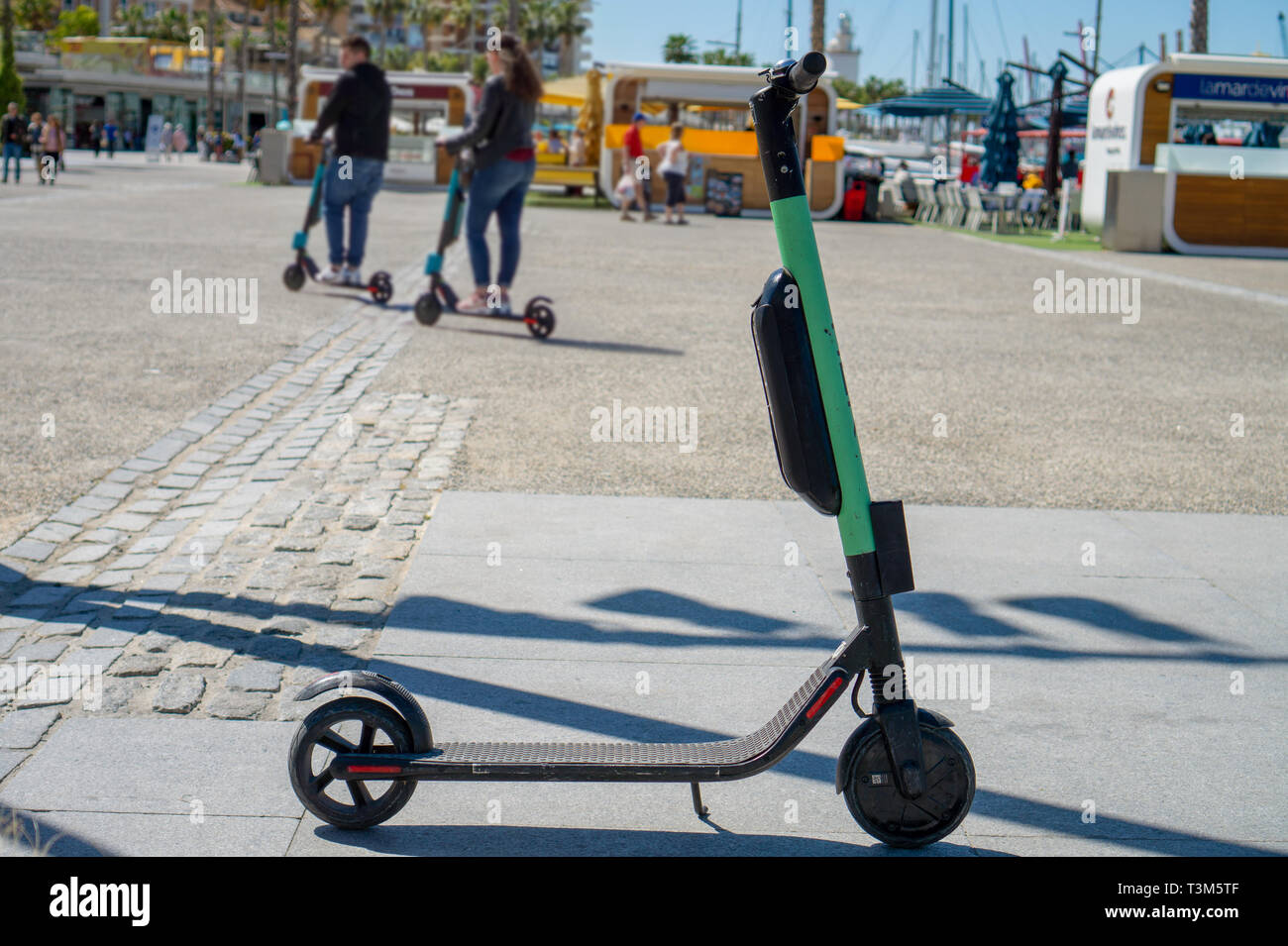 Lo scooter elettrico roller parcheggiate sul marciapiede del porto di Malaga in una giornata di sole e una offuscata giovane li utilizzano in background con i moderni mezzi di trasporto Foto Stock