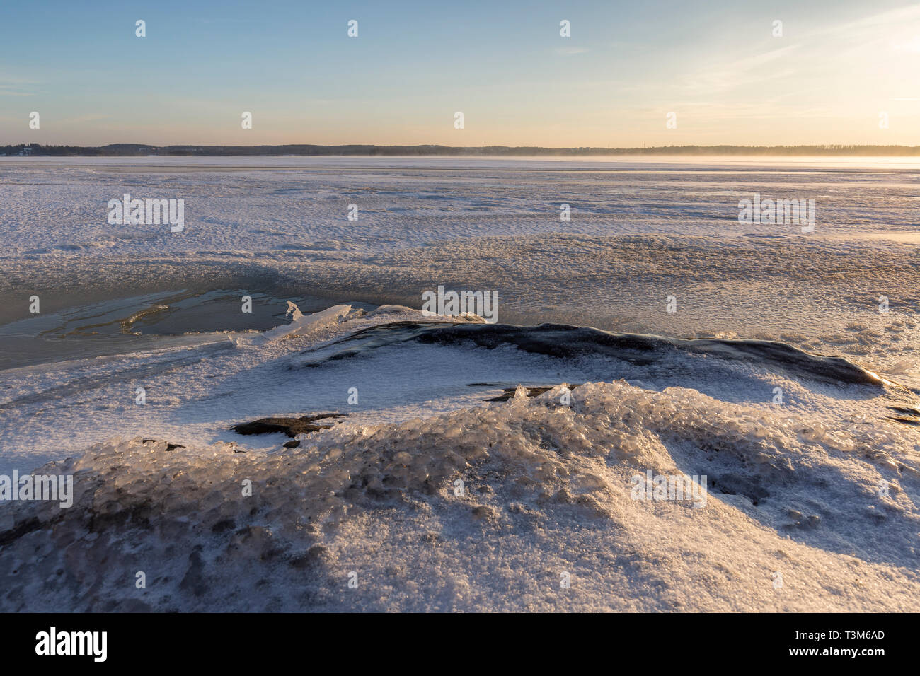 Paesaggio sereno di ghiaccio, neve, ghiaccio e roccia congelata e lago innevato in Finlandia in inverno al mattino soleggiato. Foto Stock