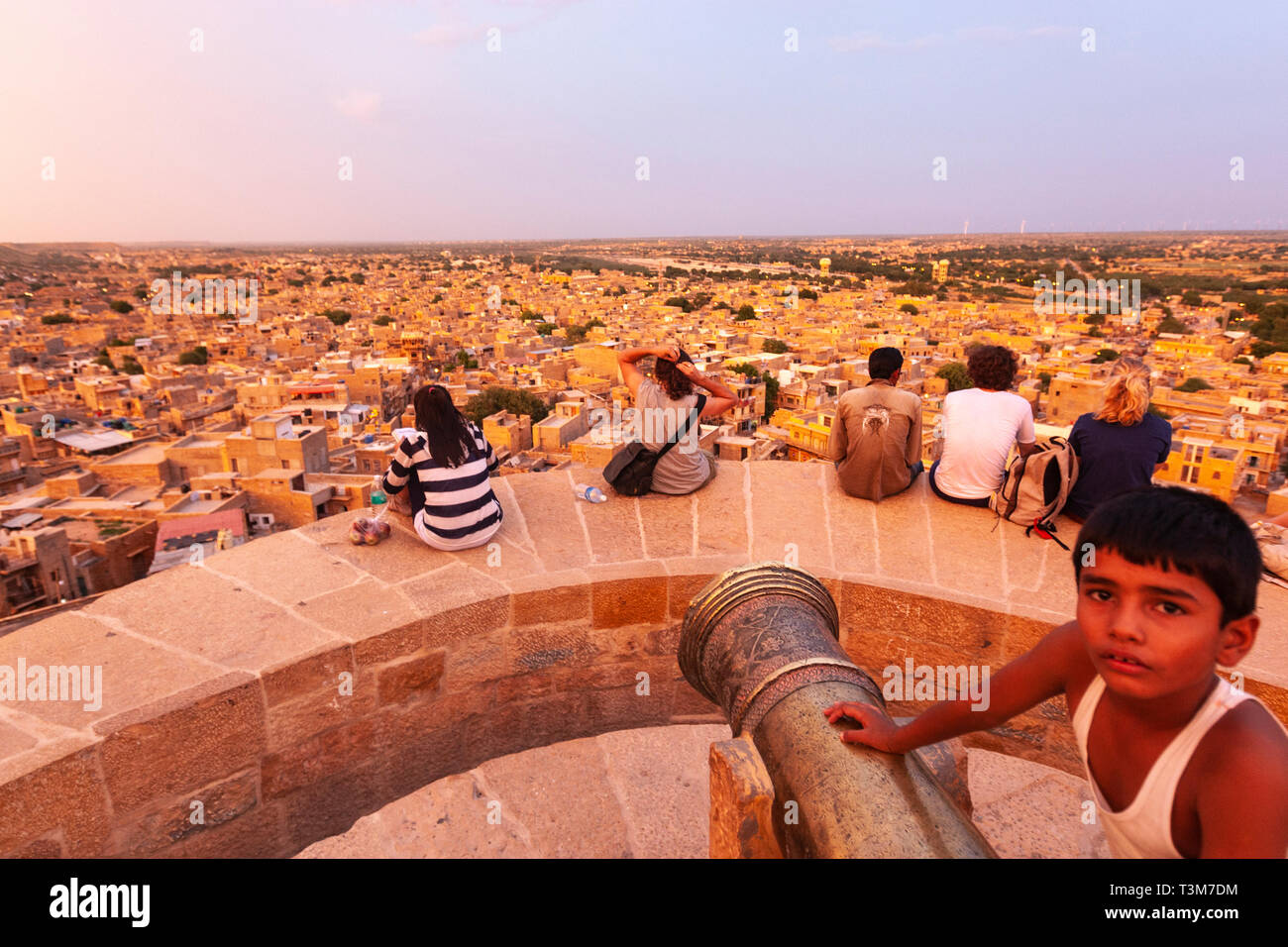 Ragazzo locale nel cannone a Jaisalmer Fort con turisti in cerca della città di Jaisalmer al tramonto, Rajasthan, India Foto Stock