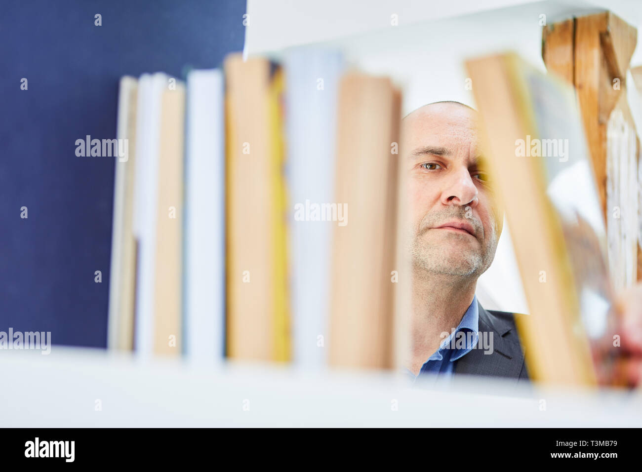 L'uomo come lettore o ordinamento bibliotecario libri o cercando un libro sullo scaffale Foto Stock