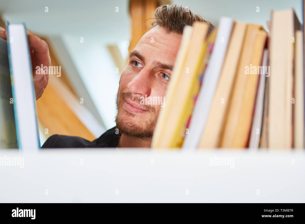 L'uomo come lettore o bibliotecario cerca un libro sullo scaffale della Biblioteca universitaria Foto Stock