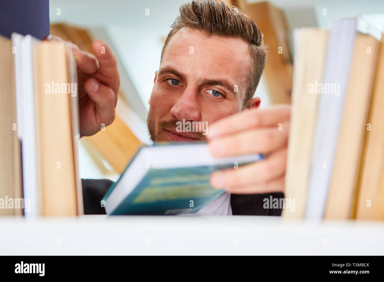 L'uomo come docente bibliotecario o cerca un libro sullo scaffale della Biblioteca universitaria Foto Stock