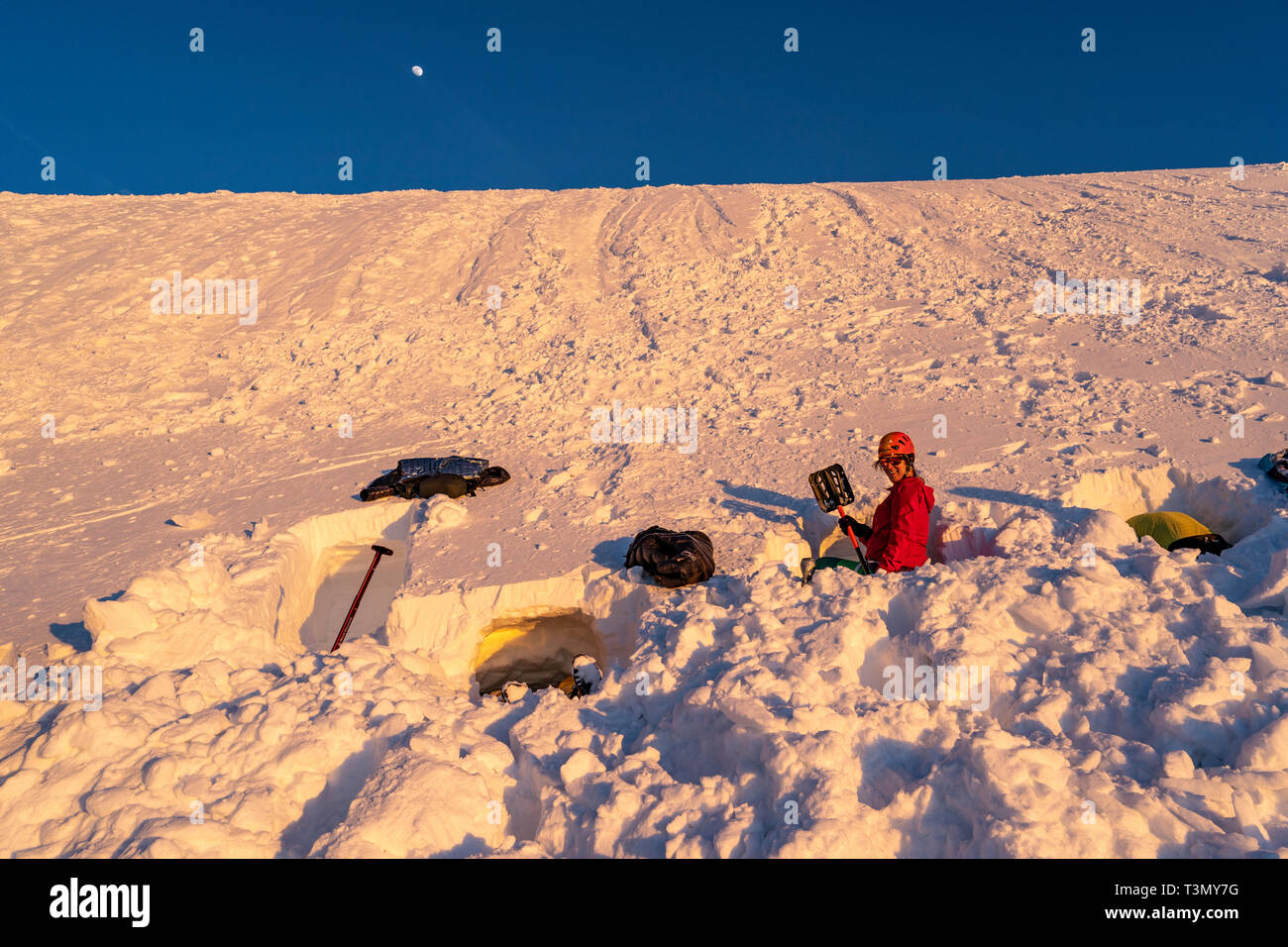 Donna spalare la neve per Bivacco accampamento al tramonto Foto Stock