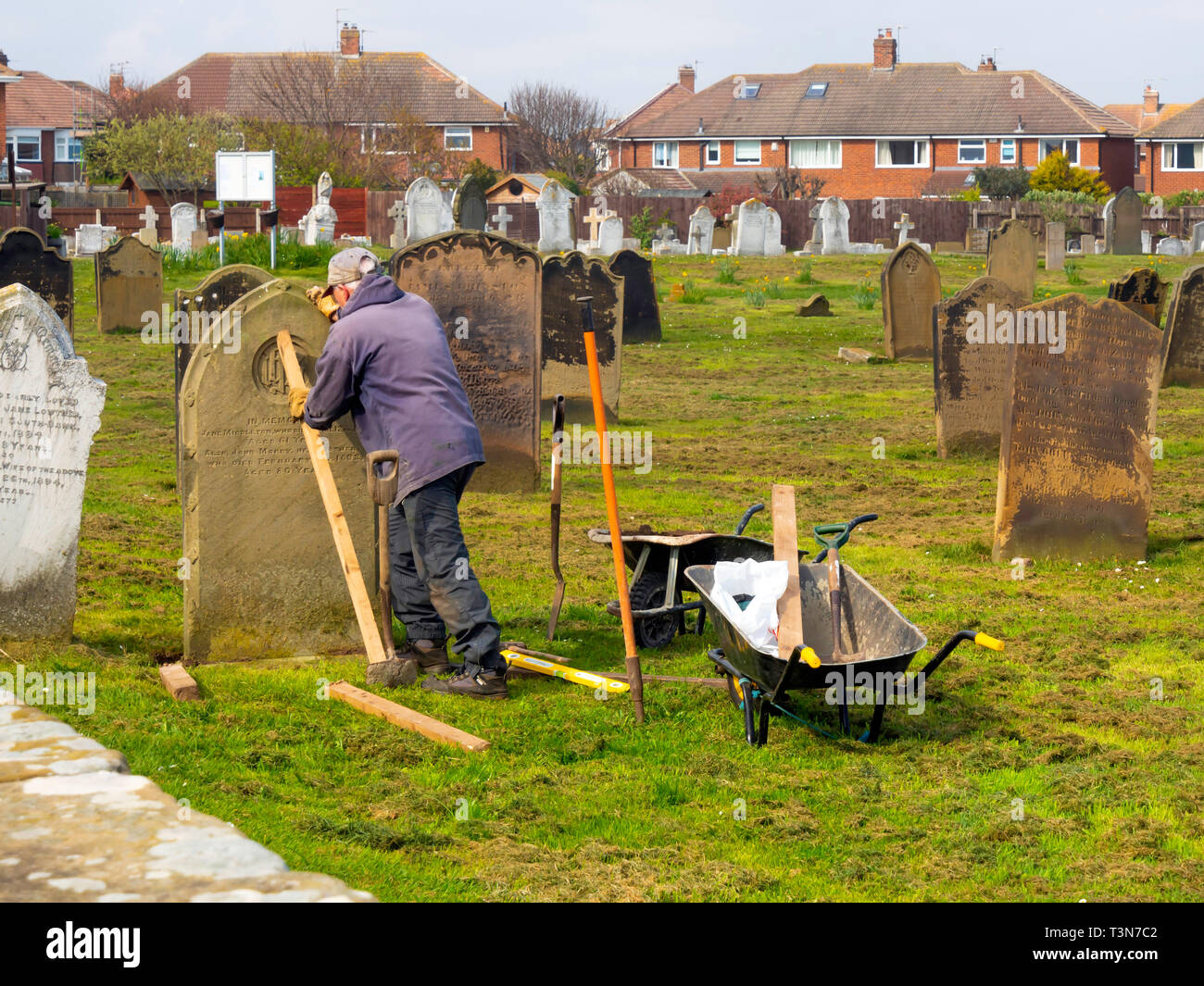 Un scalpellino al lavoro re-erigendo una lapide caduti nel cimitero di St Germains Churcyard Marske dal Sea North Yorkshire England Regno Unito Foto Stock