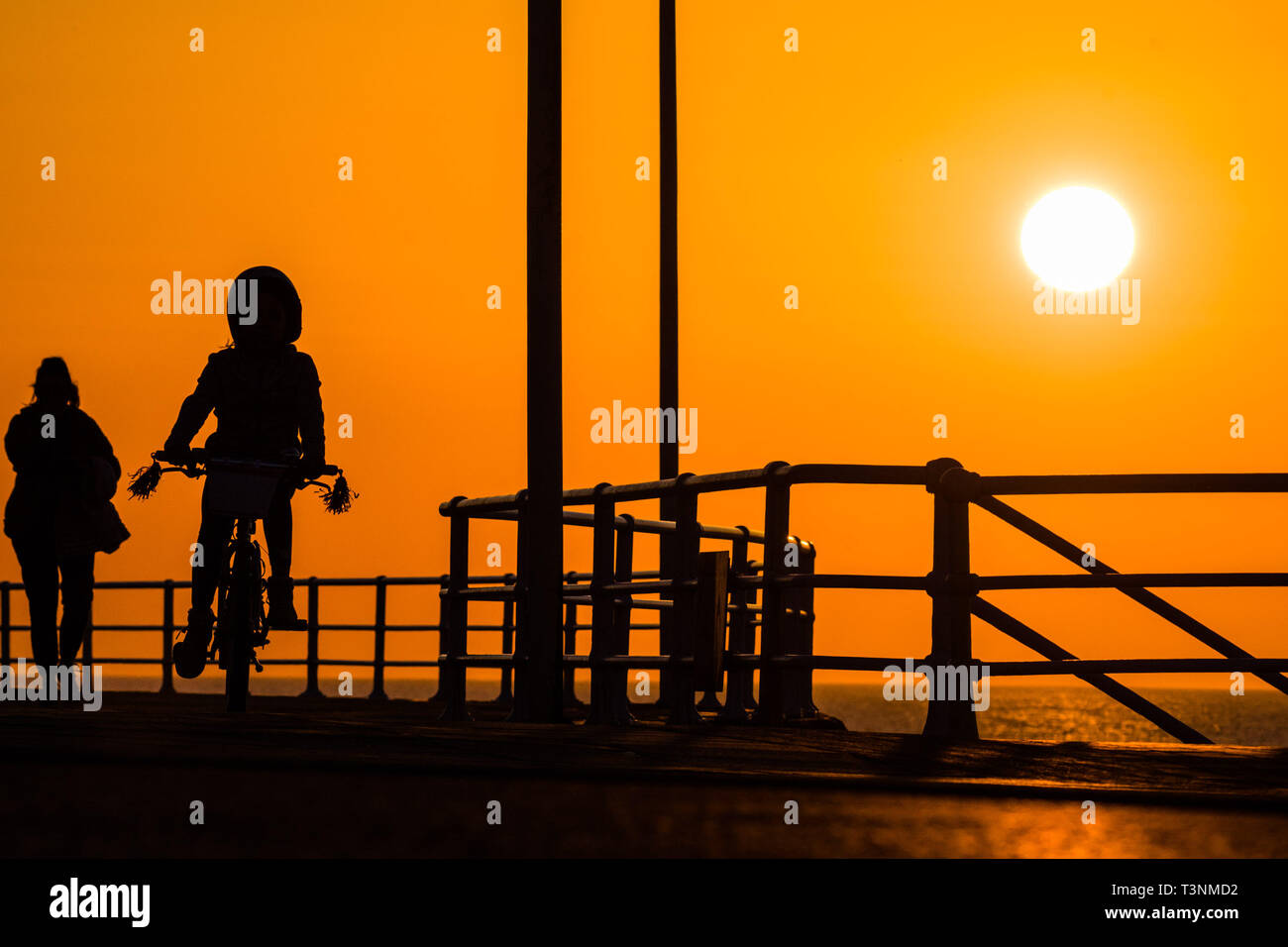 Aberystwyth, UK. Decimo Apr, 2019. Regno Unito: meteo alla fine di una giornata ininterrotte blu del cielo e il caldo sole primaverile, il sole tramonta spettacolarmente dietro le sagome delle persone a piedi lungo la passeggiata in Aberystwyth su Cardigan Bay costa del Galles occidentale. Credito: keith morris/Alamy Live News Foto Stock
