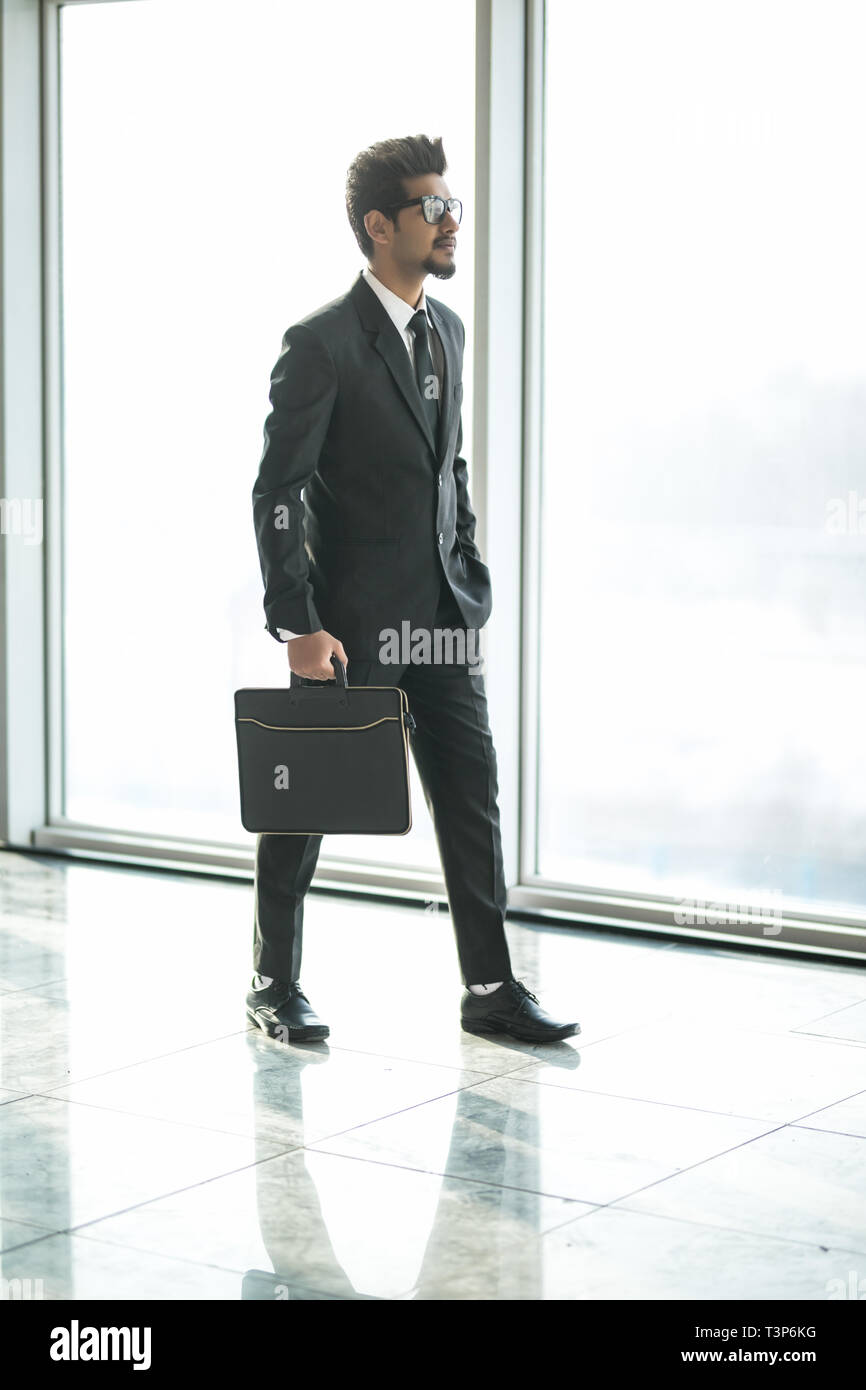 Commerciante indiano a piedi in ufficio interno con grandi finestre con vista sul centro business Foto Stock
