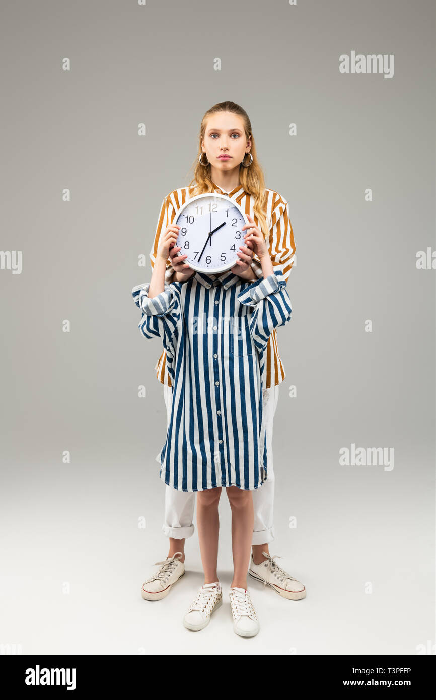 Ragazza a sovradimensionare striped shirt chiudendo il suo volto con orologio rotondo Foto Stock