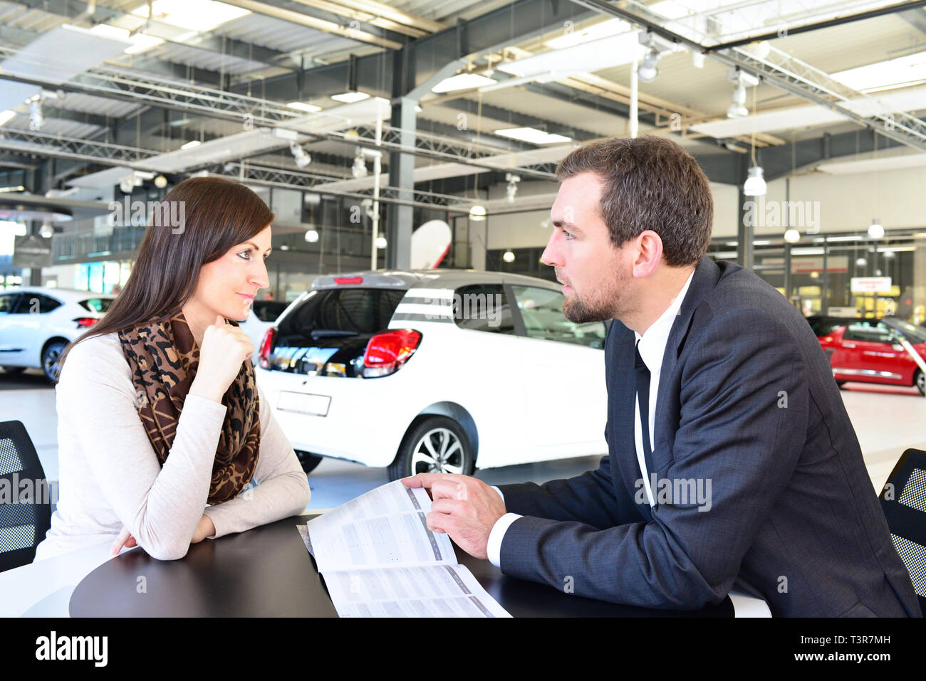 Coppia giovane l'acquisto di una nuova auto nello showroom di una concessionaria auto - firma del contratto di vendita con il venditore Foto Stock