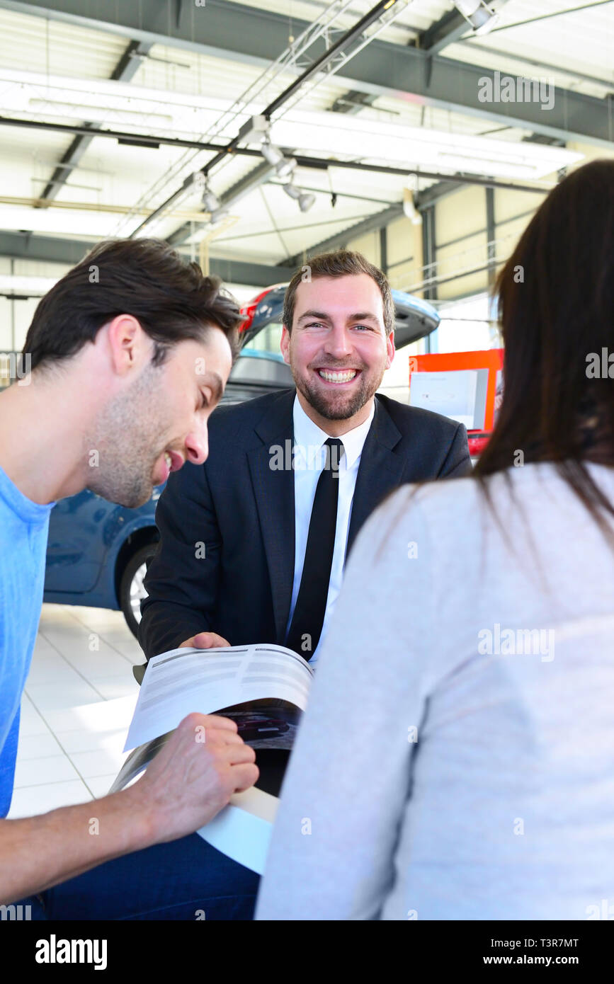 Coppia giovane l'acquisto di una nuova auto nello showroom di una concessionaria auto - firma del contratto di vendita con il venditore Foto Stock