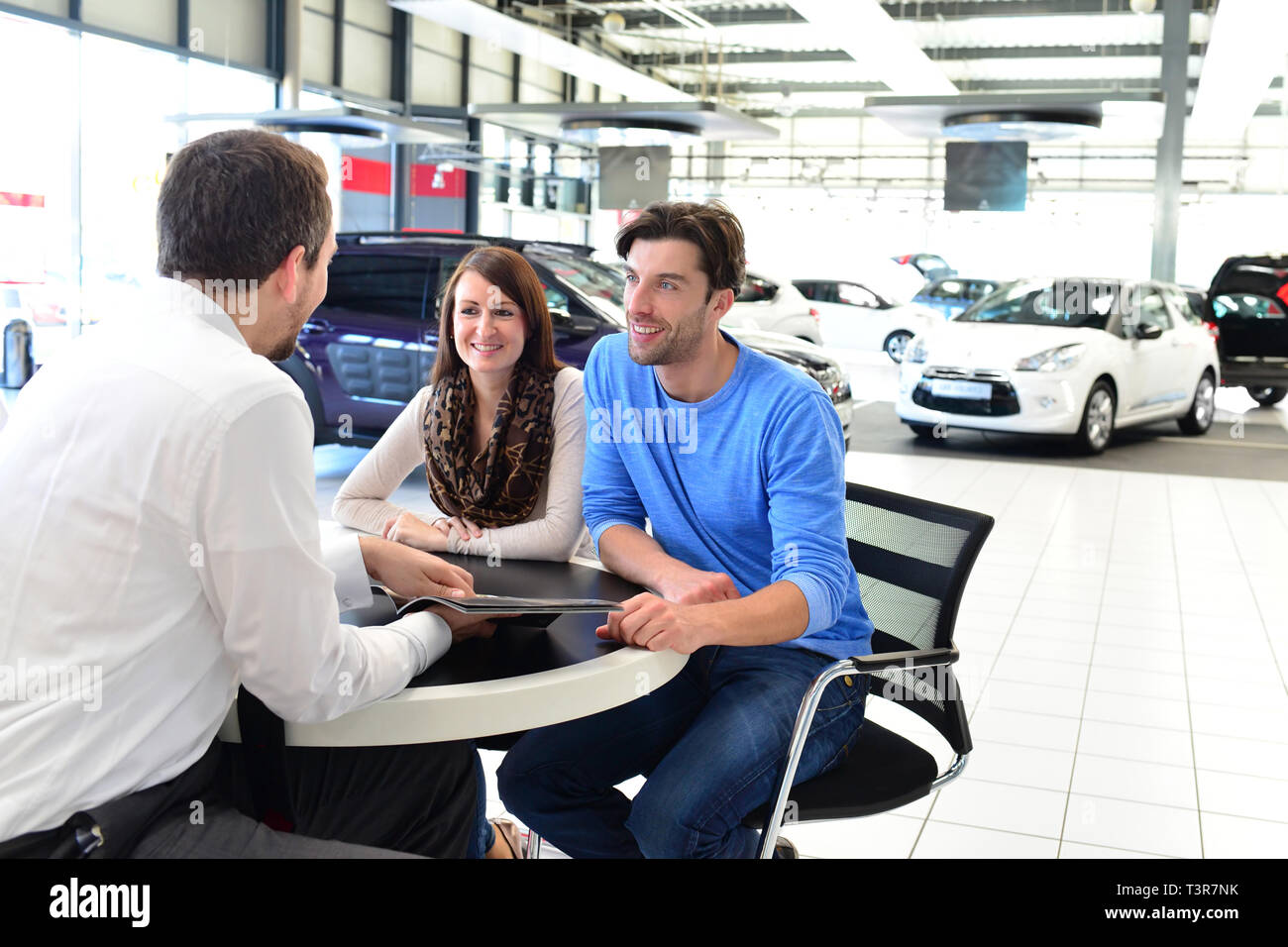 Coppia giovane l'acquisto di una nuova auto nello showroom di una concessionaria auto - firma del contratto di vendita con il venditore Foto Stock