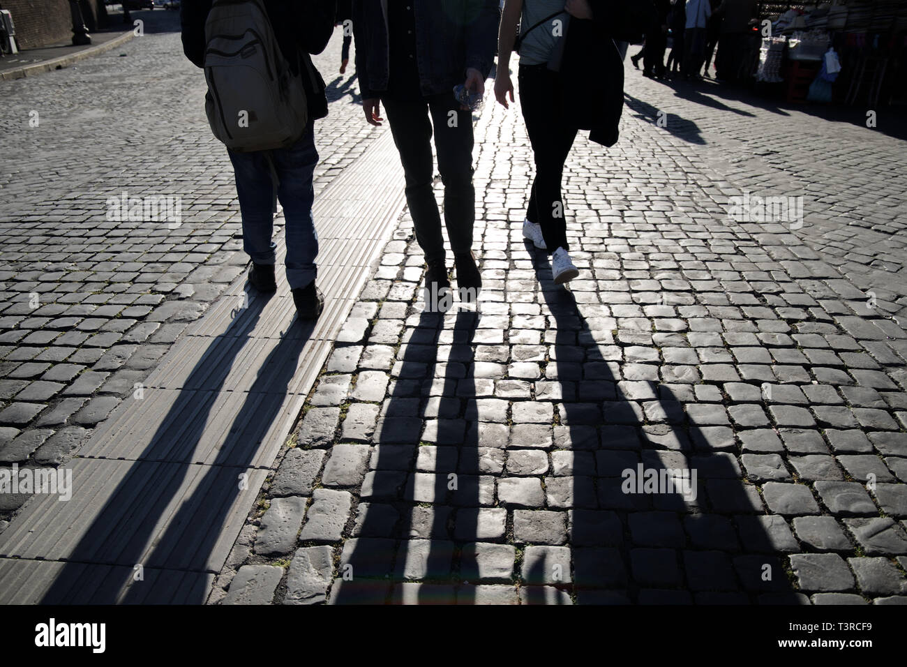 Sagome di camminare di più persone gambe sul terreno in ciottoli in controluce comprese le biciclette fotografato vicino al Vaticano a Roma Italia Foto Stock