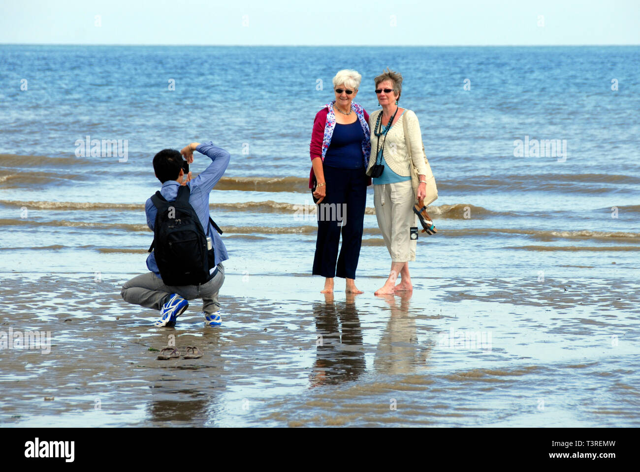 Giovane uomo prendendo fotografia di due anziane signore pagaiando sulla spiaggia Foto Stock
