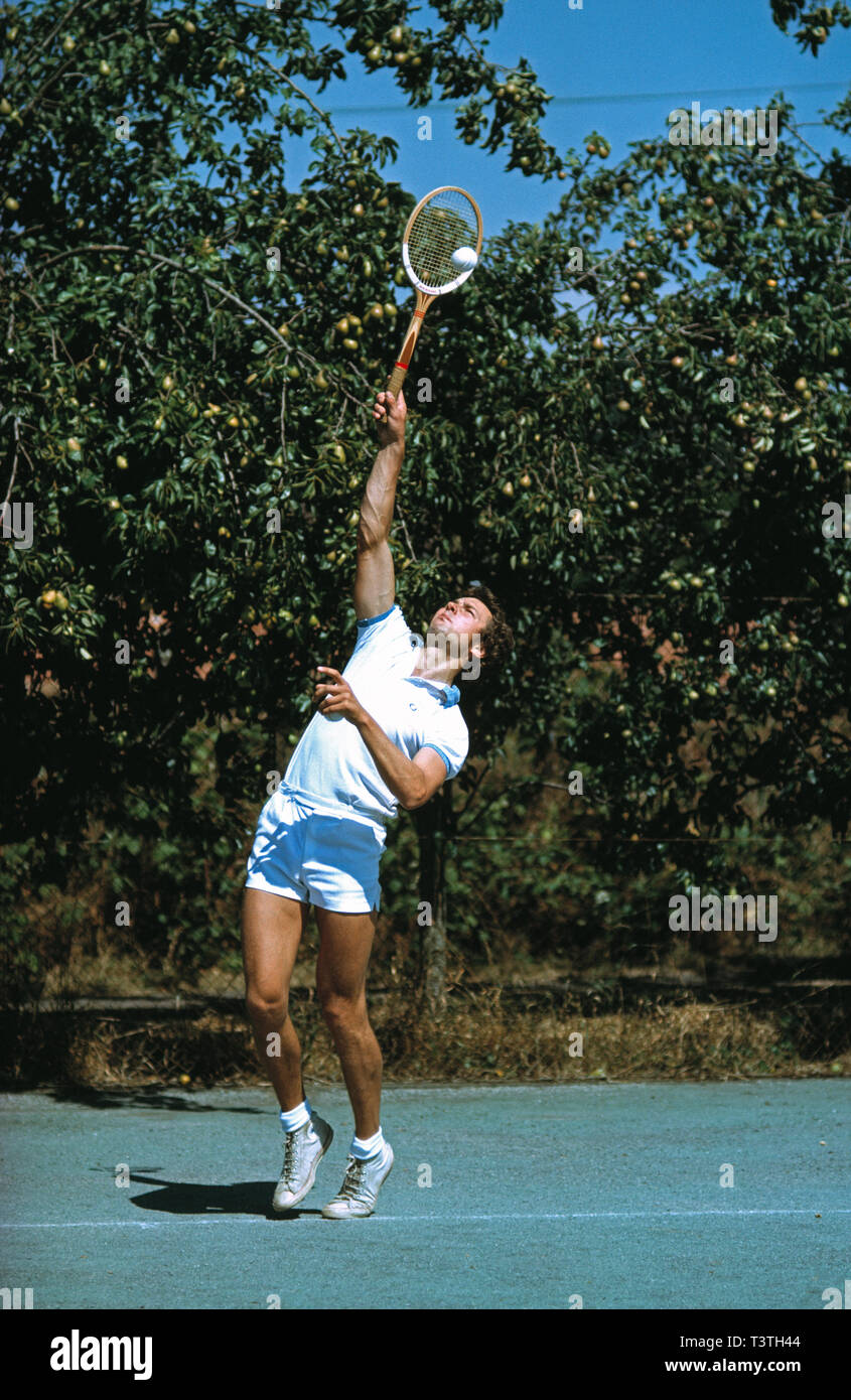 Giovane uomo giocando a tennis su corte privata. Gioco di servizio.Negli anni settanta. Foto Stock