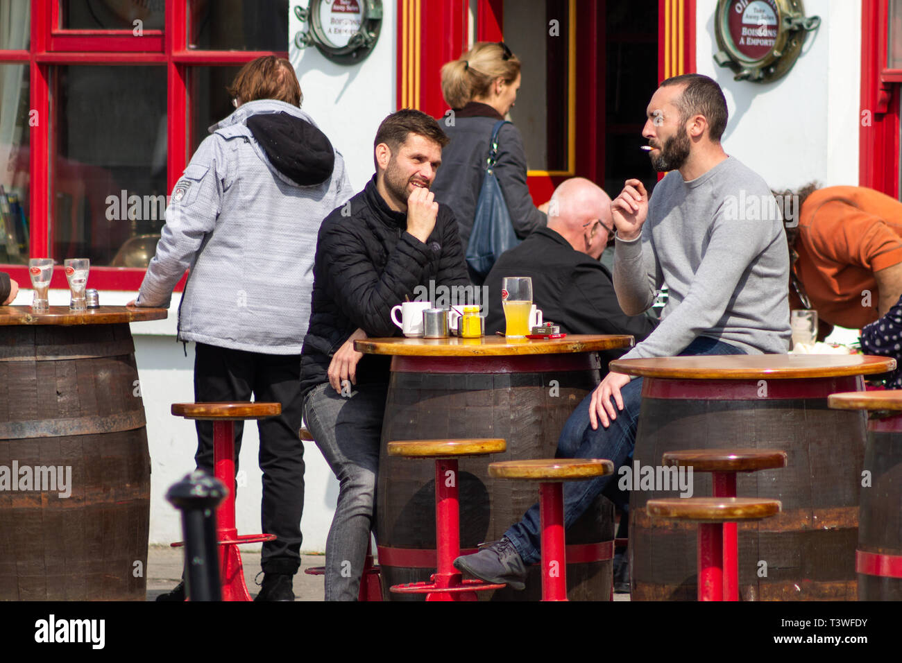 Gruppo misto di persone che vivono al di fuori di un pub gustando un drink. Irlanda, West Cork, baltimore Foto Stock