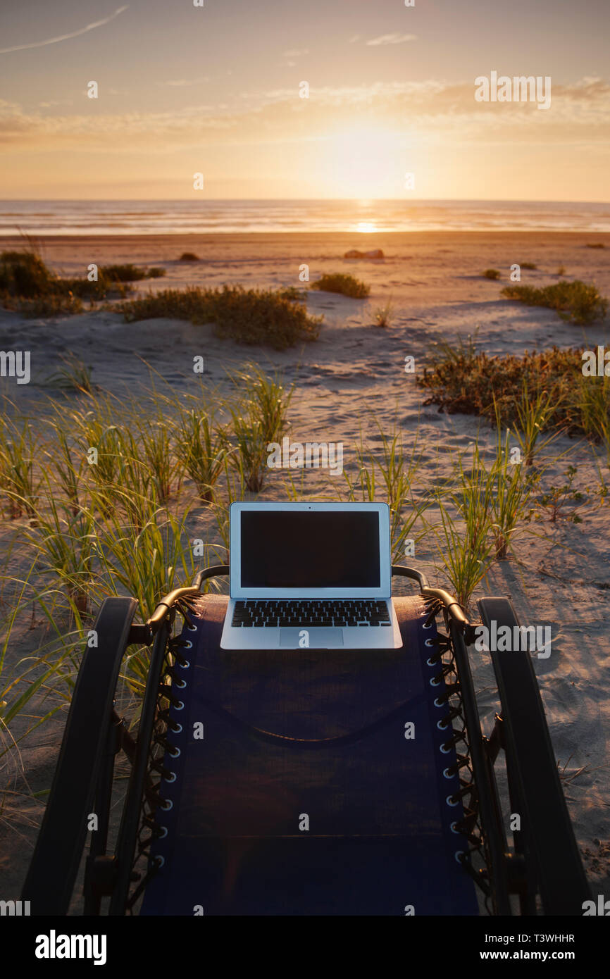 Portatile su sedia a sdraio affacciato sul tramonto sulla spiaggia Foto Stock