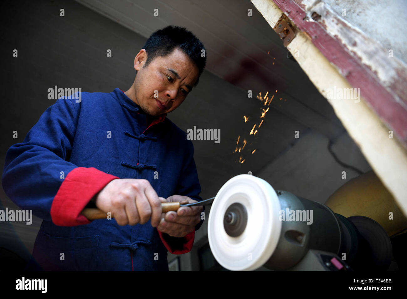 (190412) -- JINGXIAN, 12 aprile 2019 (Xinhua) -- 45 enne Ding Yonggang, un ereditiere di intaglio del legno, acuisce il suo coltello nella contea di Jingxian, est cinese della provincia di Anhui, 12 aprile 2019. Influenzato dagli anziani che sono impegnati nella lavorazione del legno, Ding ha sviluppato un forte interesse per le tradizionali tecniche di scultura sin dalla sua infanzia. Dopo anni di apprendimento e di pratica, Ding Yonggang è andata maturando nella sua abilità di sculture in legno e ha creato un gran numero di sculture in legno di opere d'arte. Sotto Ding il coltello, materie prime come alcuni umili rami e radici sono dotati di valore artistico Foto Stock
