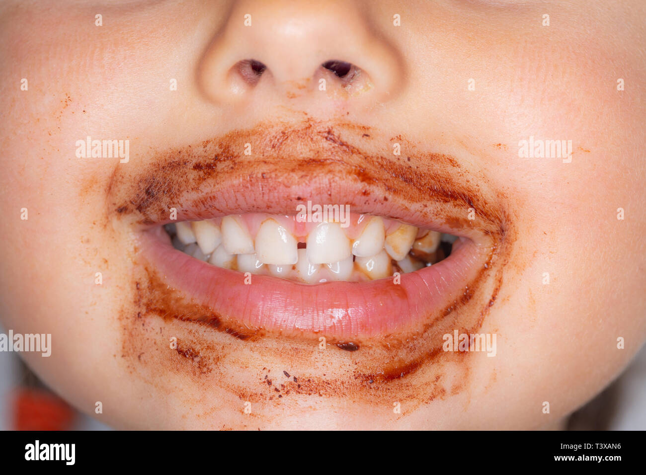 Primo piano della giovane ragazza ridere a mangiare una barretta di cioccolato con cioccolato sul suo viso Foto Stock
