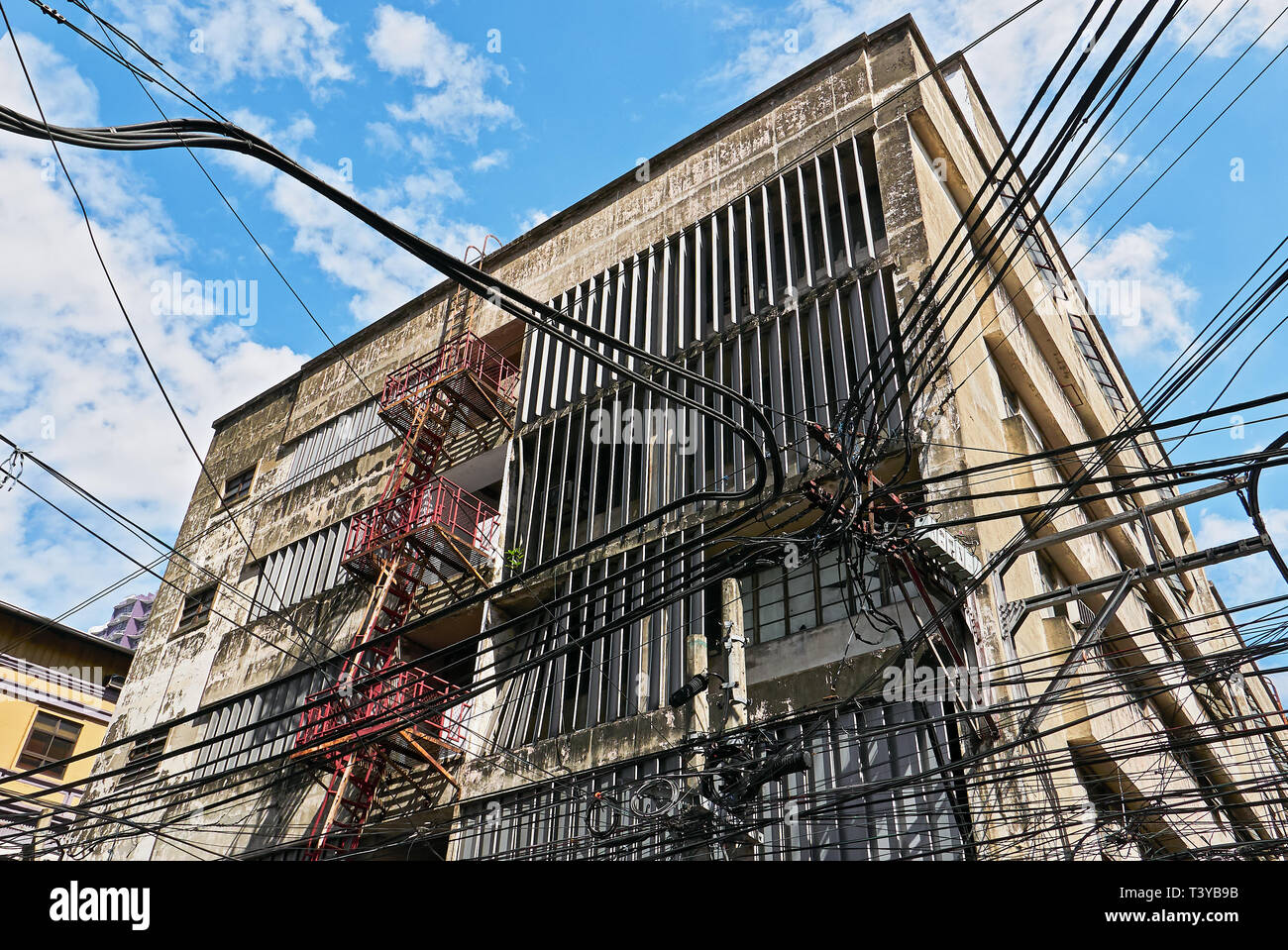 A basso angolo di visione di un vecchio alto edificio aziendale e un pasticcio di cavi e linee di alimentazione in prevalentemente cinese Binondo distretto, Manila, Filippine Foto Stock