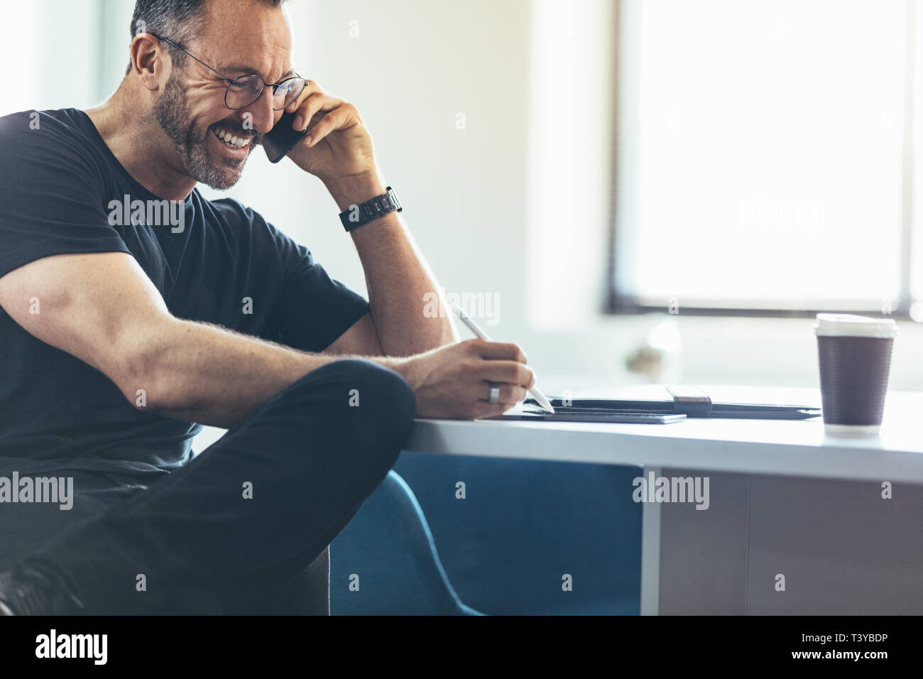 Imprenditore parlando al cellulare e al lavoro sul suo digitale compressa mentre è seduto alla sua scrivania. Imprenditore parlando al cellulare e sorridente in ufficio Foto Stock