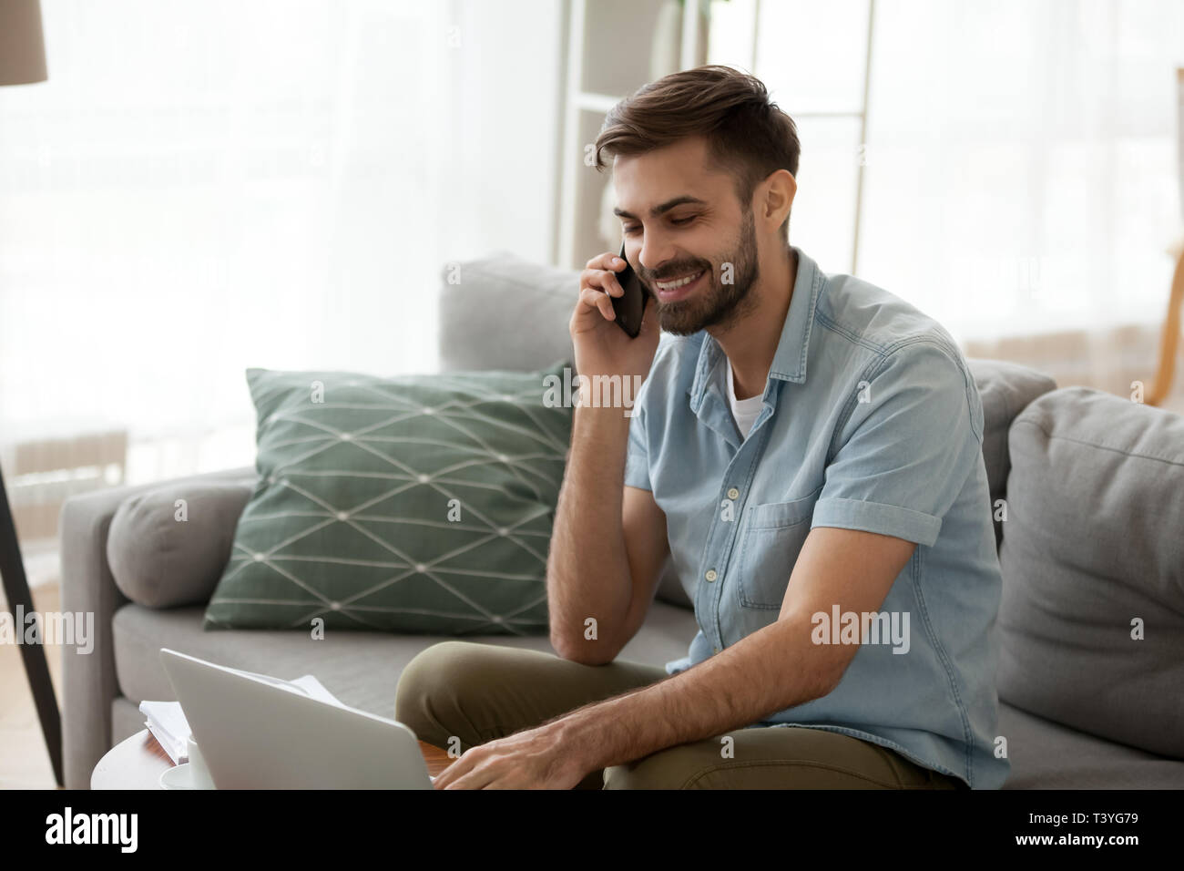 Sorridendo felice l'uomo utilizzando laptop e parlando al telefono di casa Foto Stock
