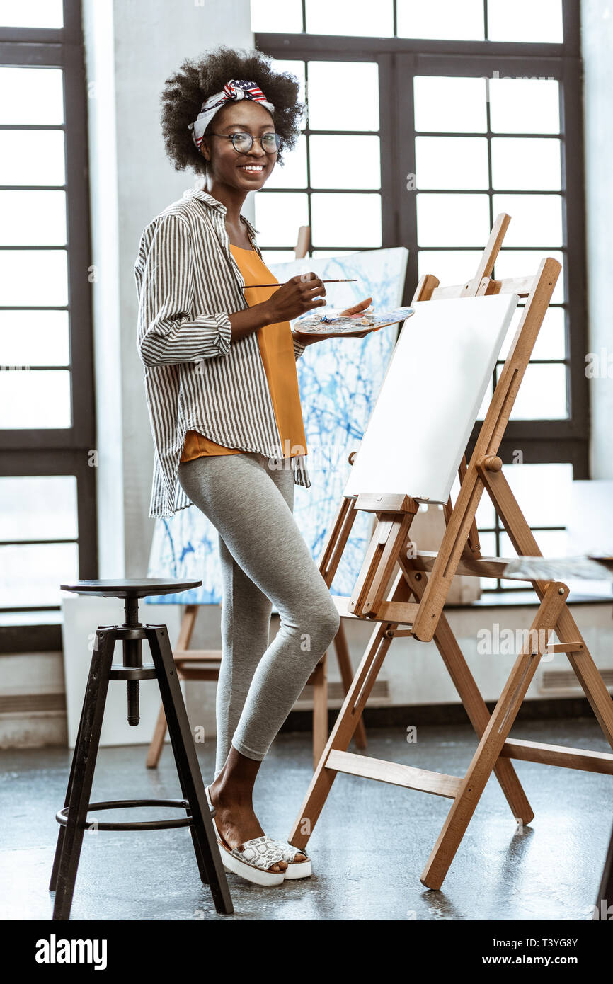 Artista in gambali. Slim giovane artista afro-americano che indossa gambali in piedi vicino al cavalletto di disegno Foto Stock