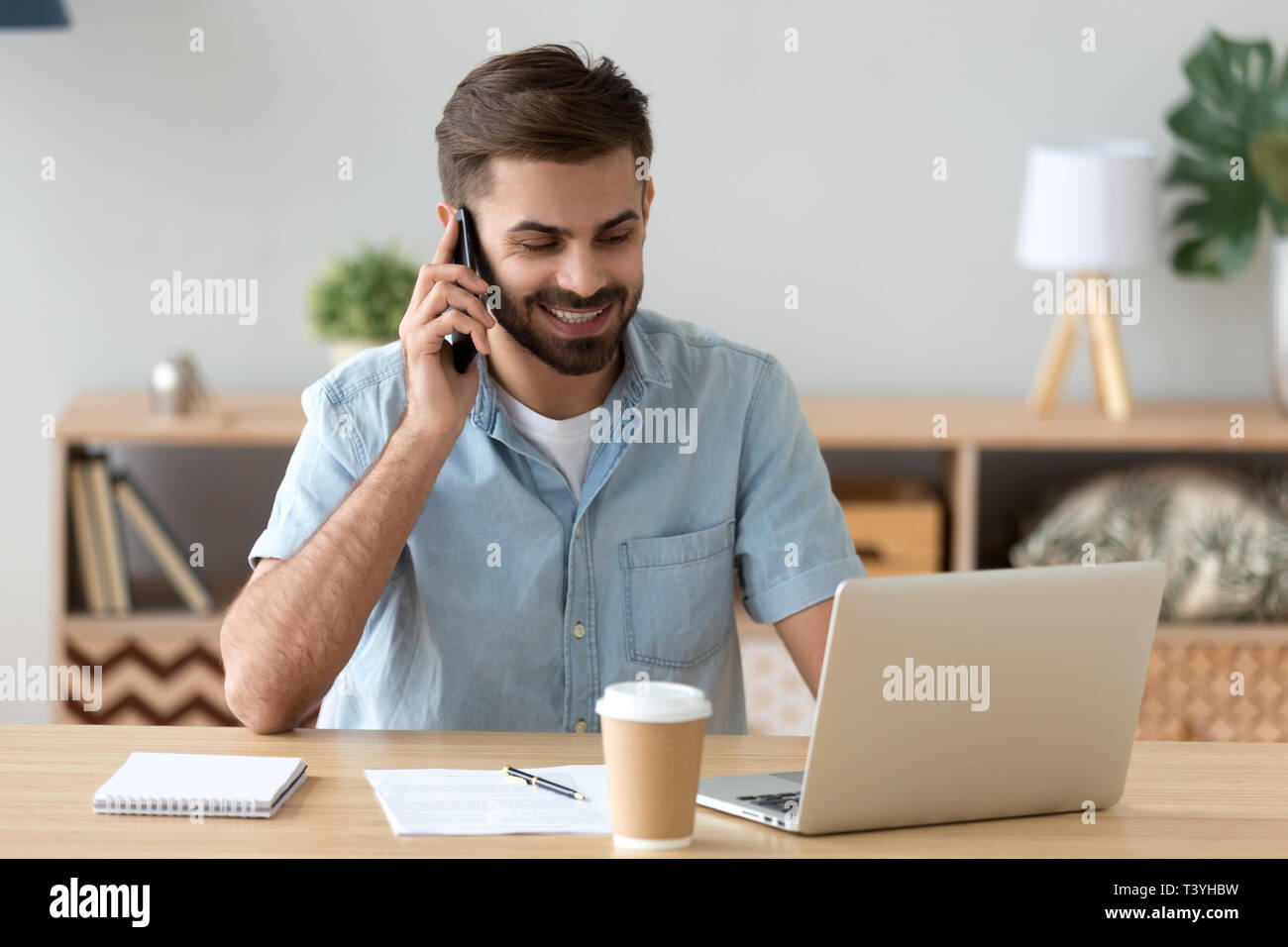Sorridere soddisfatto uomo che parla al telefono e utilizzando il portatile in ambiente di lavoro Foto Stock