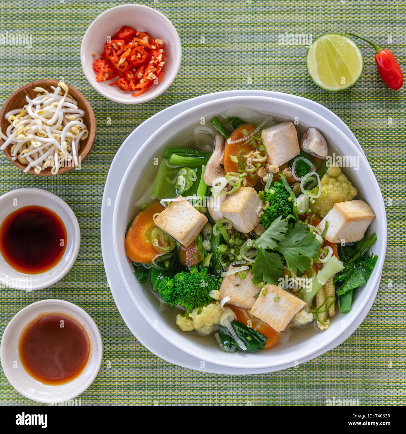 Vegetariano vietnamita noodle soup Pho servita in bianco ciotola rotonda con salse, calce, peperoncino e germogli di legumi. Bacchette di legno sul lato. Vista dall'alto. Foto Stock