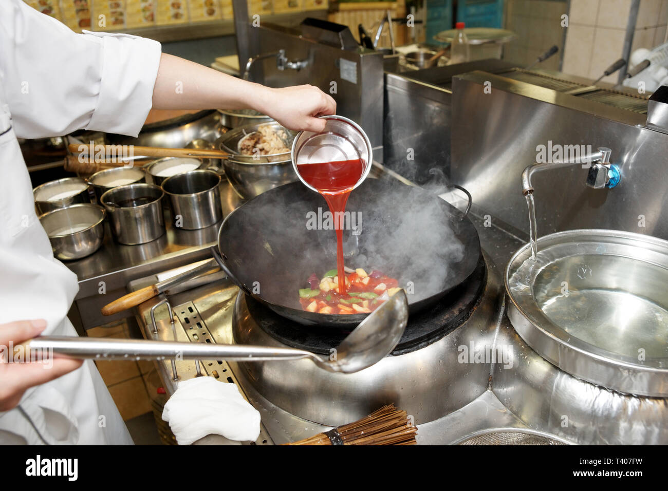 Lo chef è colata di salsa acida in un wok a livello commerciale kirchen Foto Stock
