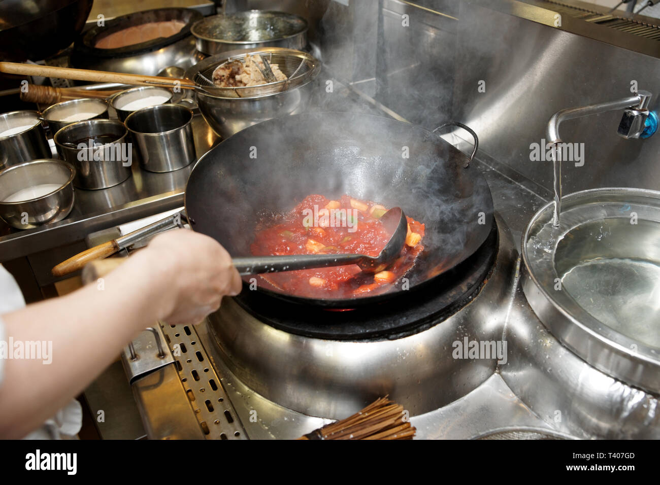Lo chef è agitazione di verdure con salsa acida in un wok a livello commerciale kirchen Foto Stock