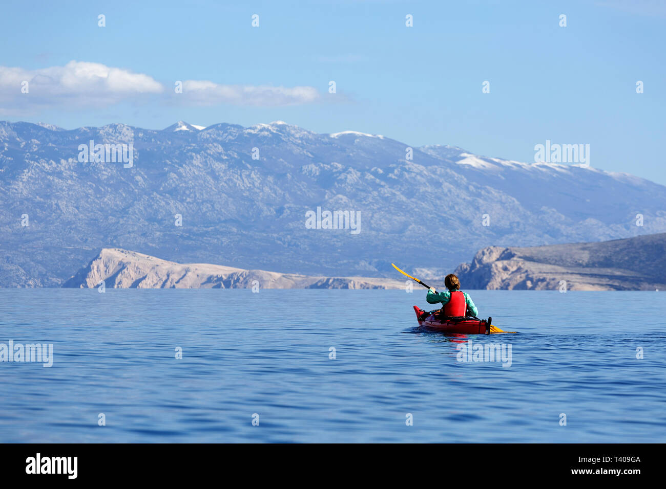 Donna kayak tra belle isole croate, montagna Velebit in background, Croazia, Krk. Foto Stock