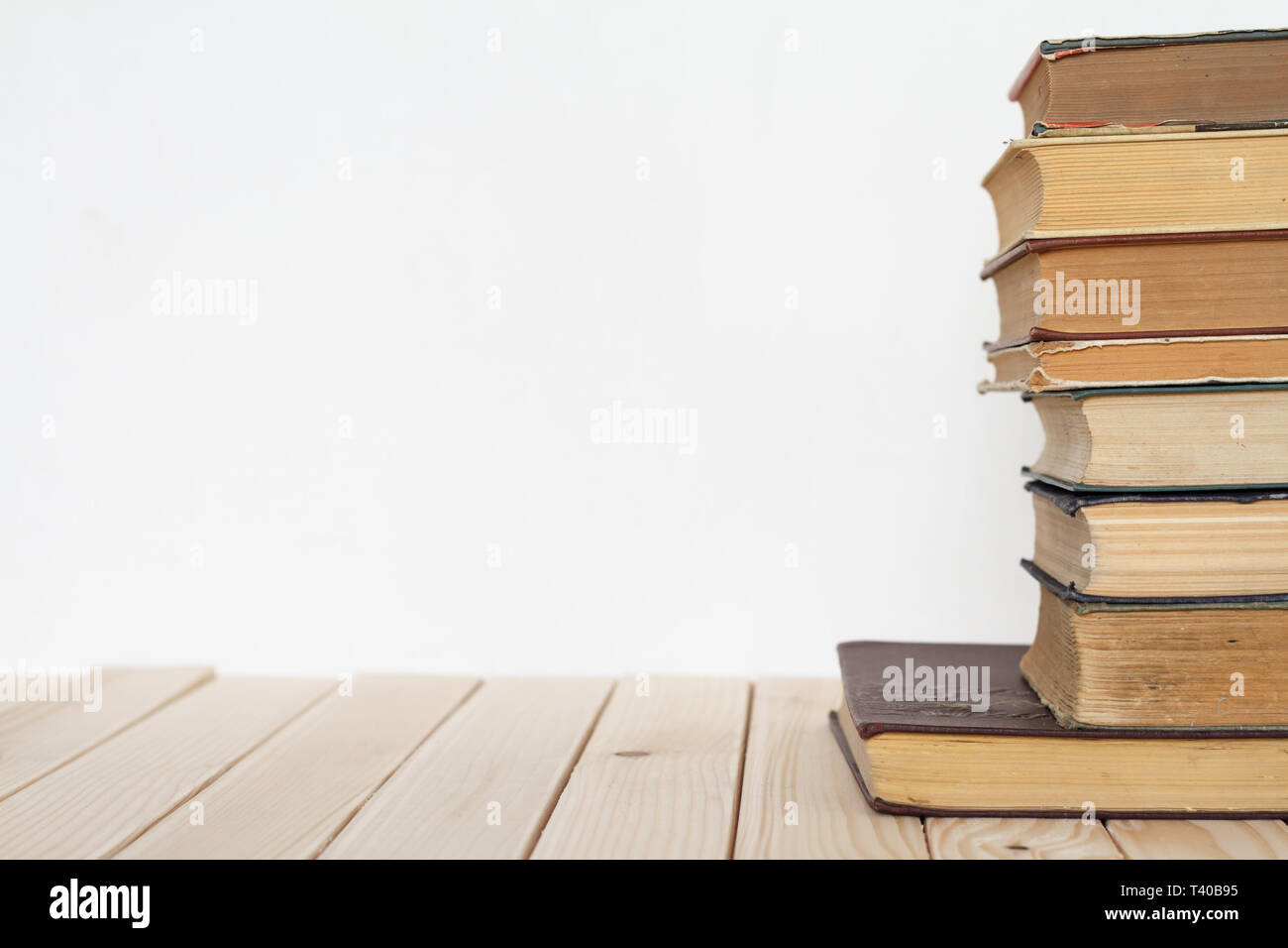 Una pila di libri d'epoca per il business e l'istruzione su una superficie di legno contro un muro bianco, torna al concetto di scuola. Foto Stock