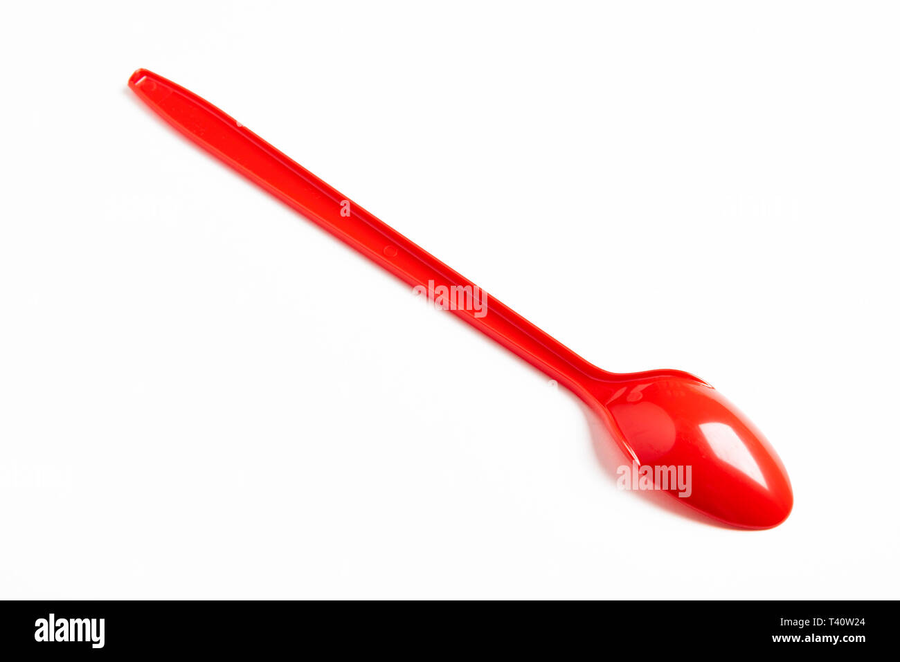 Un rosso lucido in plastica lungo cucchiaio artisticamente impostato su sfondo bianco con spazi negativi. Foto Stock