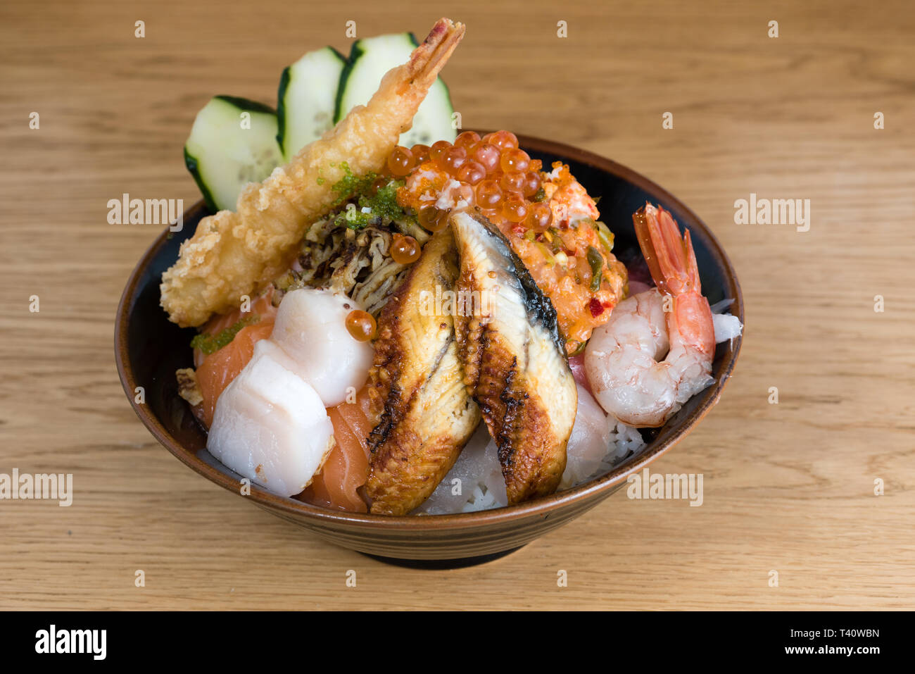Tipica giapponese donburi pesce, gamberi tempura, materie gamberetti, filetti di salmone, tonno grigliato, caviale e tartare di tonno, a fette cetrioli, materie branzino filetti Foto Stock