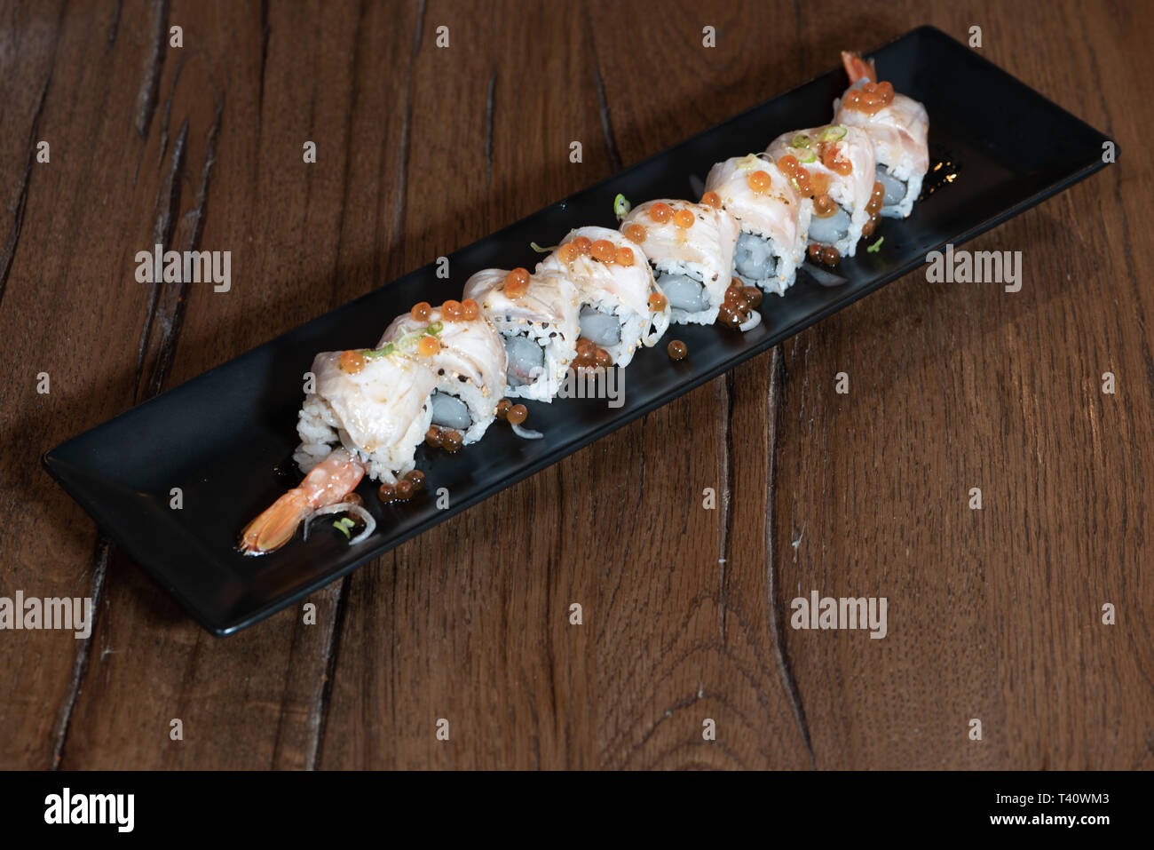 Uramaki speciale con gamberi crudi, spigola, cipolle, Ikura, salsa Ponzu, legno scuro dello sfondo della tabella Foto Stock