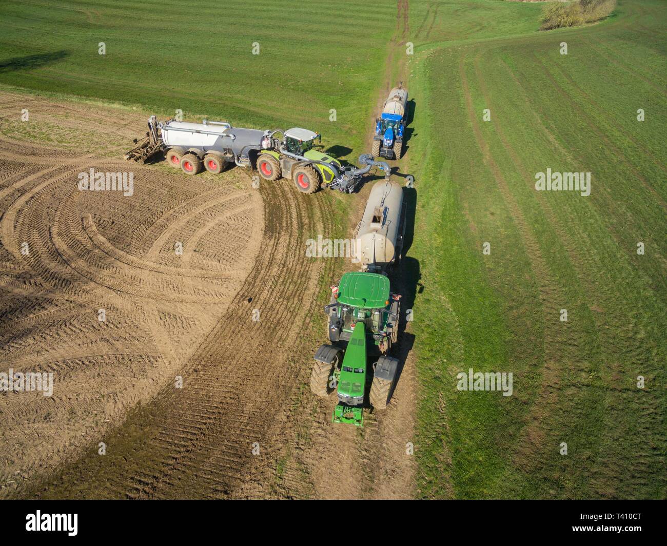 Vista aerea di un trattore con un moderno rimorchio di fertilizzante e un secondo trattore con un fertilizzante liquido il rimorchio su un campo agricolo Foto Stock