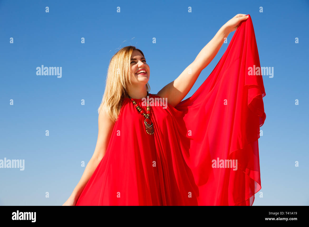 Donna bionda in abito rosso sul cielo blu sullo sfondo. Foto Stock