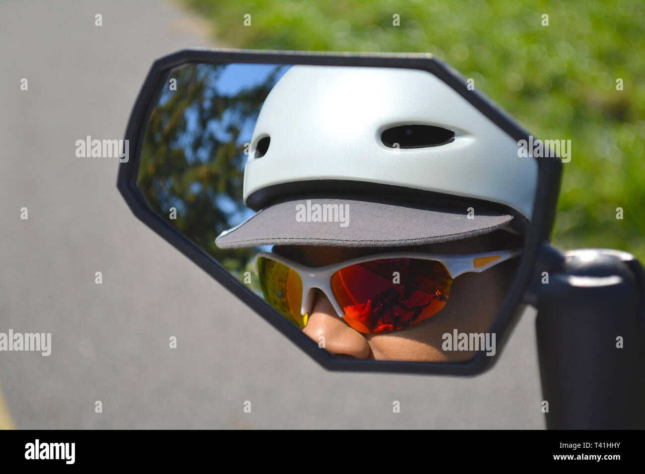 La riflessione di donna faccia in bicicletta a specchio. Ciclista femmina rider in occhiali da sole con casco bianco riflesso nello sport e bike specchio. Close up. Foto Stock