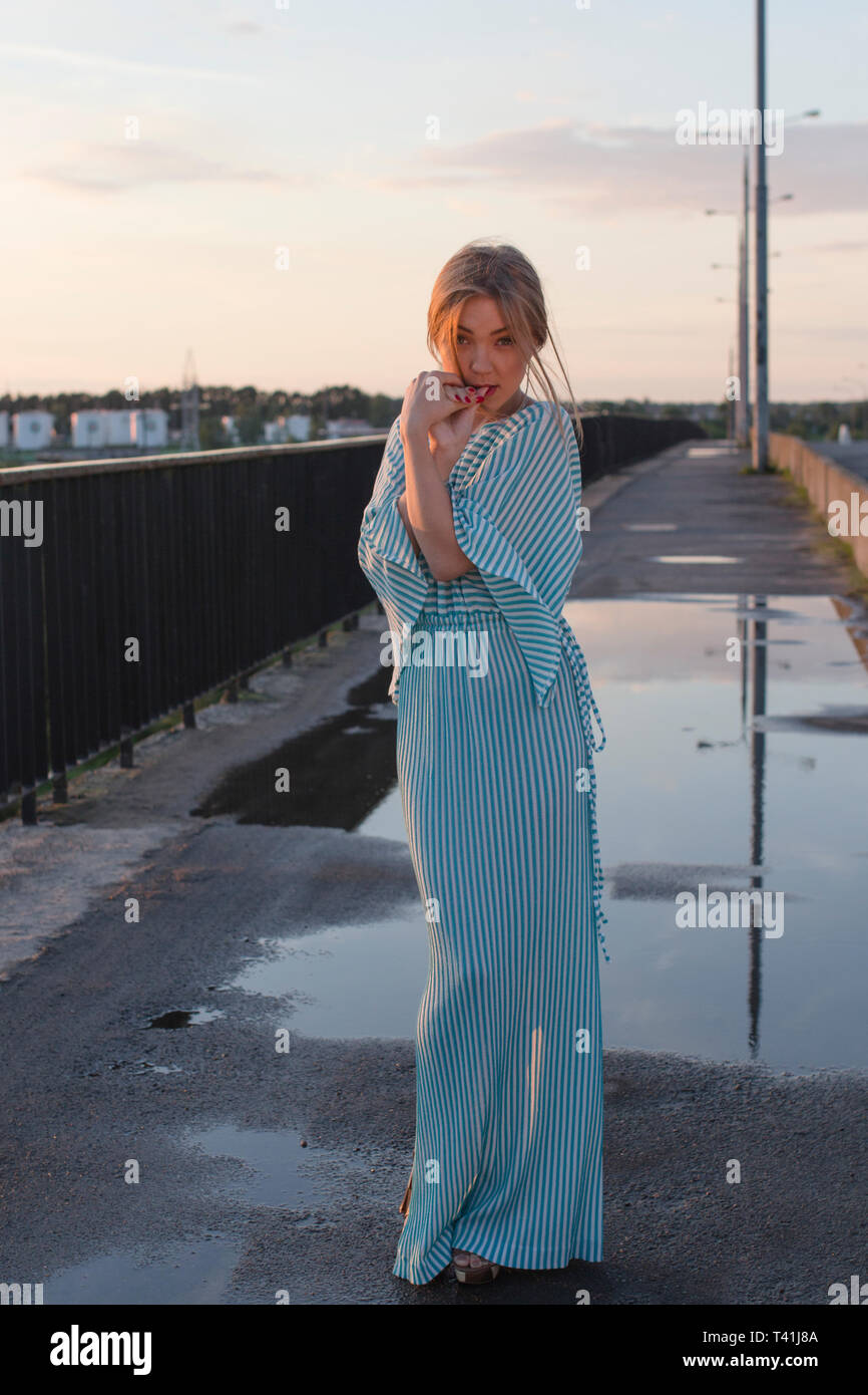 Una donna sta in un abito lungo sul ponte durante il tramonto. Foto Stock