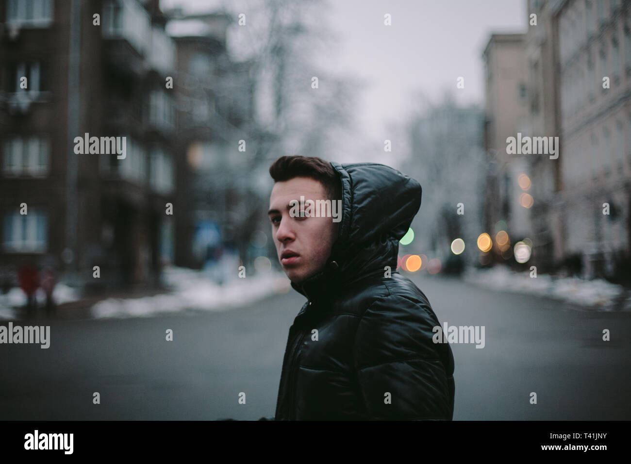 Vista laterale del giovane uomo attraversando una strada di città in inverno Foto Stock