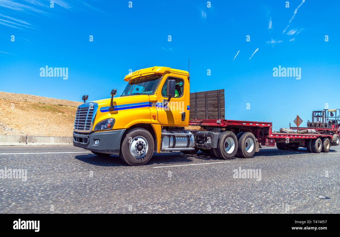 Giallo big rig cabina giorno semi carrello per locali e regionali di consegna con fase di vuoto verso il basso semi rimorchio e il carrello elevatore montato alla estremità del rimorchio in esecuzione Foto Stock