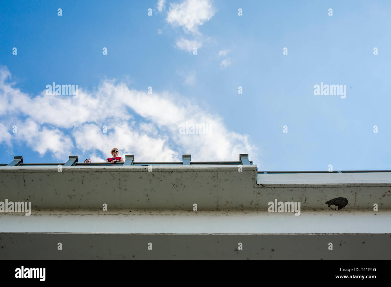 La vista dal di sotto di un cielo blu e due persone di sbirciare da dietro un ponte Foto Stock