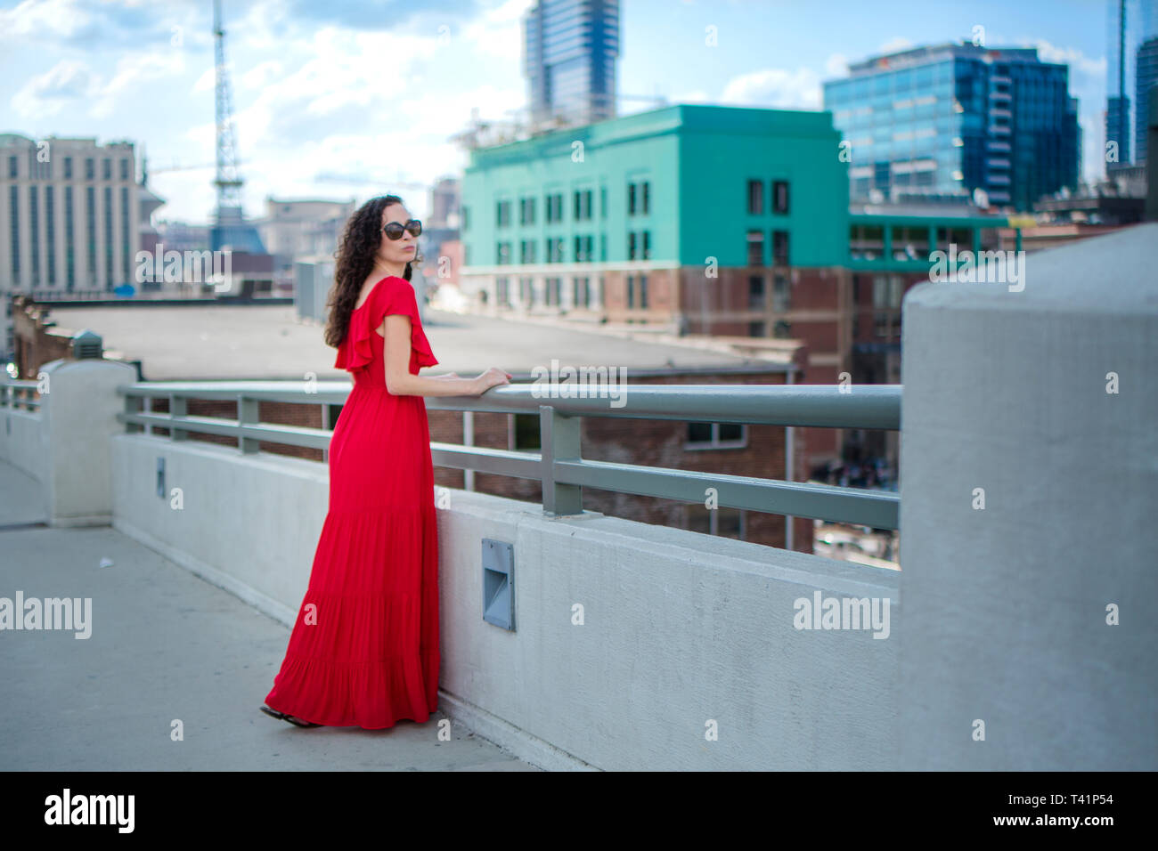 Una bella donna sorge in un lungo abito rosso contro una skyline della città Foto Stock